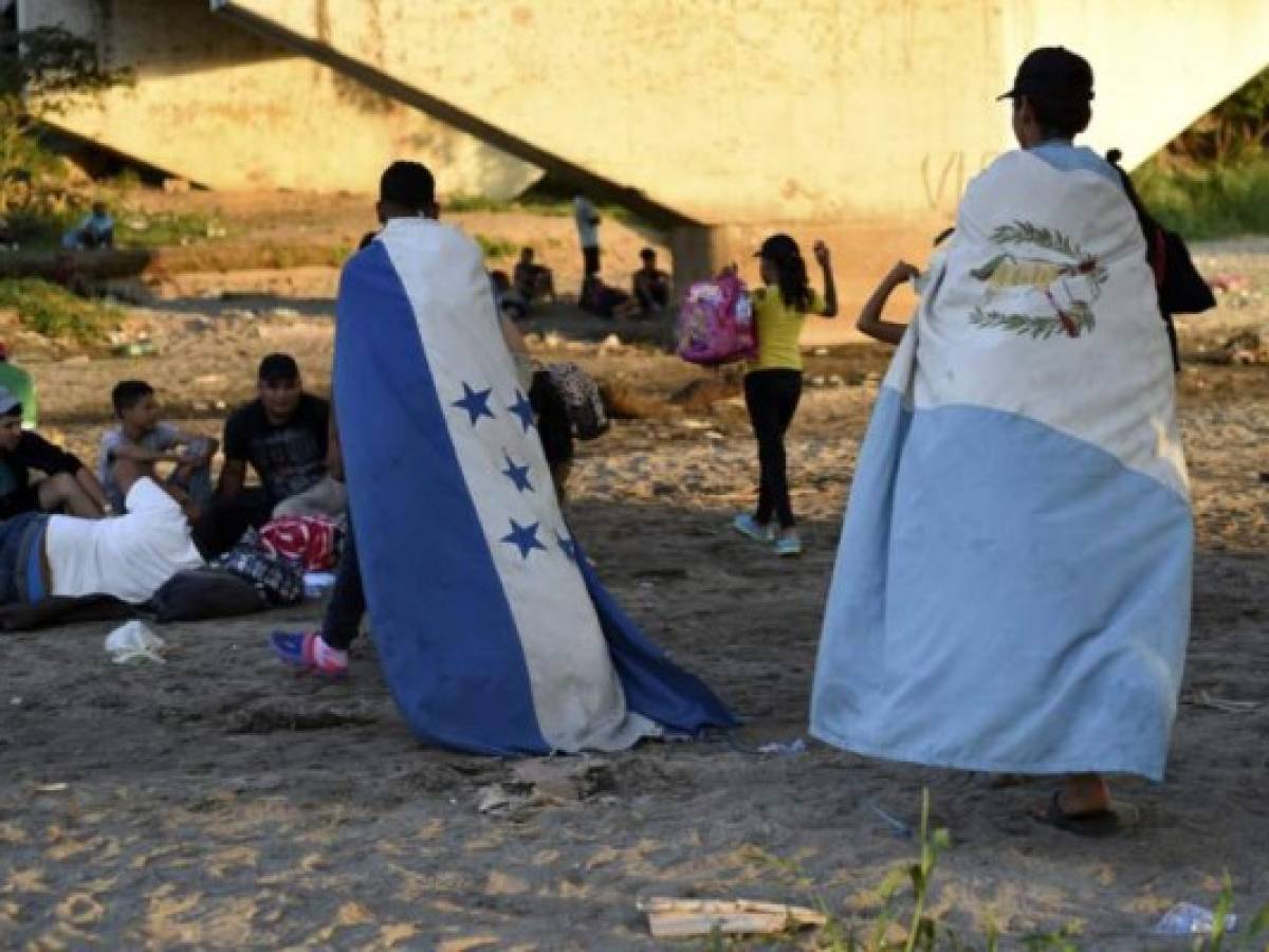 Migrants wearing a Honduran (L) and a Guatemalan flag wait to cross from Tecun Uman, Guatemala, to Ciudad Hidalgo, Mexico, on January 18, 2020. - On the eve, Mexican President Andres Manuel Lopez Obrador offered 4,000 jobs to members of the caravan in an attempt to dissuade them from traveling on to the United States. The caravan, which formed in Honduras this week, currently has around 3,000 migrants, Lopez Obrador said. (Photo by Johan ORDONEZ / AFP)