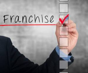 Businessman hand writing Franchise and check listing task. Isolated on grey background. Stock photo