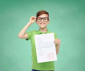 childhood, school, education and people concept - happy smiling boy in eyeglasses holding paper with test result over green school chalk board background