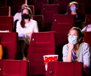 Audience at the cinema wearing protective face masks and sitting on a distance while watching the movie.