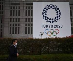 A man in a face mask walks past a display showing the Tokyo 2020 logo in Tokyo on March 23, 2020. (Photo by CHARLY TRIBALLEAU / AFP)