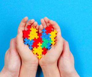 Adult and kid hands holding colorful heart on blue background. World autism awareness day concept.