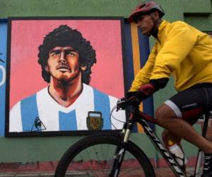 A man on bicycle passes by a mural depicting late Argentine football star Diego Maradona, in Bogota on November 23, 2021. - November 25 marks the first anniversary of Diego Maradona's death. he died from a heart attack at the age of 60. (Photo by Raul ARBOLEDA / AFP)
