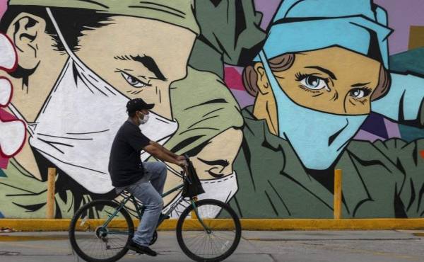A man ride sa bike past a coronavirus-related mural by urban artists Mick Martinez and 'Were Torres' in Ciudad Juarez, Chihuahua state, Mexico, on June 27, 2020. (Photo by HERIKA MARTINEZ / AFP)