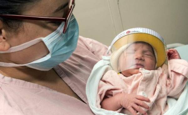 A woman wearing a face mask poses with her newborn baby -wearing a face shield- in the Neonatology unit of the Mexico Hospital in San Jose, Costa Rica, on April 28, 2020, following the implementation of strict measures to prevent the spread of the COVID-19 coronavirus. (Photo by str / AFP)