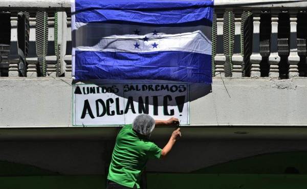 A man places a Honduran national flag and a sign reading 'United we will succeed' on the balcony of a supermarket in Tegucigalpa on April 18, 2020, amid the new coronavirus pandemic. - 46 have died out of 457 infected with COVID-19 in Honduras since the outbreak in its Central American nation. (Photo by ORLANDO SIERRA / AFP)