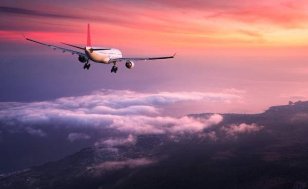 Airplane. Landscape with big white passenger airplane is flying in the red sky over the clouds at colorful sunset. Journey. Passenger airliner is landing at dusk. Business trip. Commercial plane
