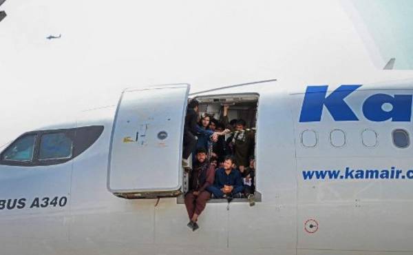 Afghan people climb up on a plane and sit by the door as they wait at the Kabul airport in Kabul on August 16, 2021, after a stunningly swift end to Afghanistan's 20-year war, as thousands of people mobbed the city's airport trying to flee the group's feared hardline brand of Islamist rule. (Photo by Wakil Kohsar / AFP)