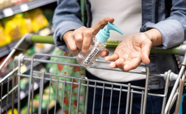 Asian shopper disinfecting hands with sanitizer in supermarket during shopping for groceries