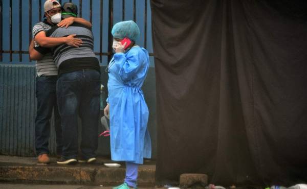 Relatives of an alleged COVID-19 victim embrace as a health worker speaks on the phone at a field hospital set up in the yard of the School Hospital in Tegucigalpa, on July 22, 2020. - At least 1,000 have died and 30,867 have been infected with COVID-19 in Honduras, amid corruption accusations against Honduran President Juan Orlando Hernandez in the purchase of seven mobile hospitals, biosecurity equipment and material. (Photo by ORLANDO SIERRA / AFP)
