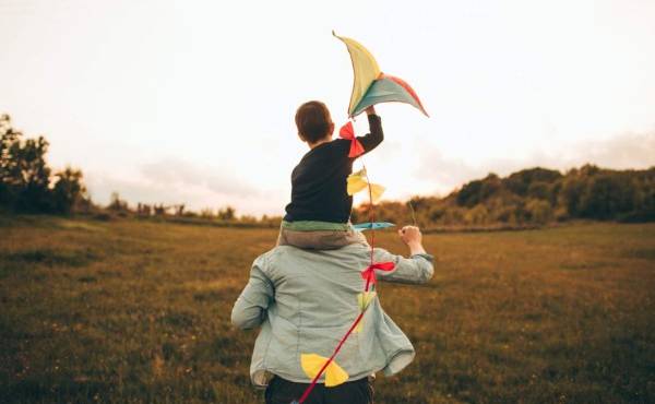 Little boy is running a kite with his father, on a beautiful day they are spending outdoors in nature