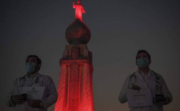 El personal médico se para frente al monumento al Divino Salvador del Mundo, que se ilumina en rojo como tributo al trabajo que realizan durante la pandemia del nuevo coronavirus. Foto por Yuri CORTEZ / AFP