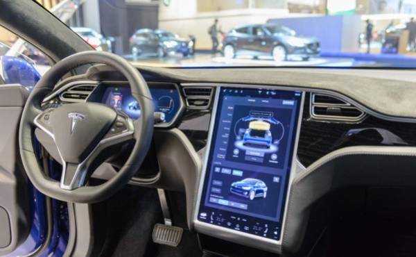 Brussels, Belgium - January 13, 2017: Luxurious interior on a Tesla Model X 90D full electric luxury crossover SUV car with a large touch screen and dashboard screen. The car is fitted with leather seats and aluminium details. The Model X uses falcon wing doors for access to the second and third row seats. The car is displayed on a motor show stand, with lights reflecting off of the body. There are people looking around and other cars on display in the background.
