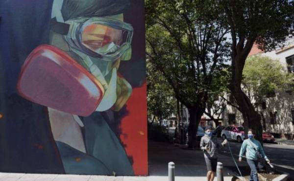 People walk next to a coronavirus-related mural at the Roma neighborhood in Mexico City, on June 9, 2020, during the novel COVID-19 pandemic. (Photo by ALFREDO ESTRELLA / AFP)
