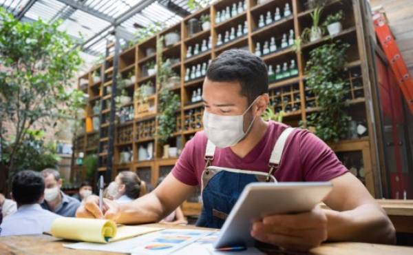Portrait of a business manager doing the books at a restaurant wearing a facemask during the COVID-19 pandemic - reopening of business
