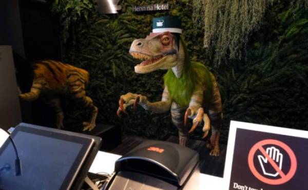 A robot dinosaur wearing a bellboy hats welcomes guests from the front desk at the Henn-na Hotel in Urayasu, suburban Tokyo on August 31, 2018. The reception at the Henn-na Hotel east of Tokyo is eeriely quiet until customers near the robot dinosaurs manning front desk. Their sensors detect motion and they bellow: 'Welcome.' It might be about the weirdest check-in experience possible, but that's exactly the point at the Henn-na ('Weird') chain, which bills itself as offering the world's first hotels staffed by robots. / AFP PHOTO / Kazuhiro NOGI