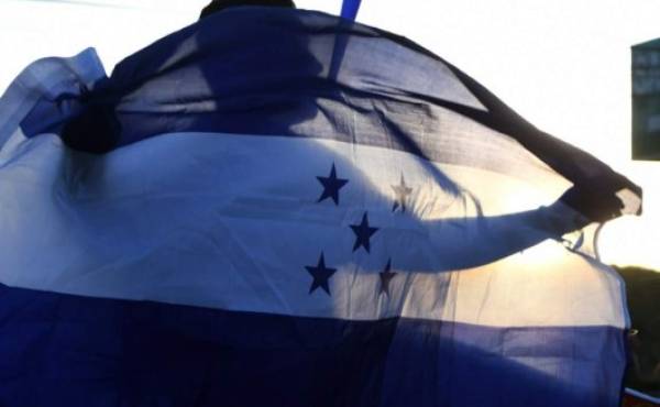 A supporter of opposition party Libertad y Refundacion (LIBRE) holds a Honduran national flag during a protest in demand of a reduction in the price of fuel in Tegucigalpa on July 27, 2018. Transport unions threaten with going again on strike if the price of fuel is not reduced. / AFP PHOTO / ORLANDO SIERRA