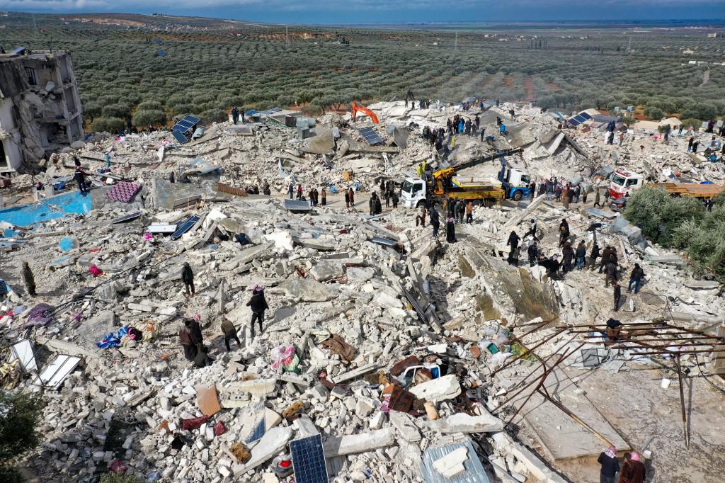 <i>Esta vista aérea muestra a los residentes, ayudados por equipos pesados, buscando víctimas y sobrevivientes entre los escombros de los edificios derrumbados luego de un terremoto en la aldea de Besnia, cerca de la ciudad de Harim, en la provincia noroccidental de Idlib en Siria, controlada por los rebeldes, en la frontera con Turquía. el 6 de febrero de 2022. (Foto de Omar HAJ KADOUR / AFP)</i>